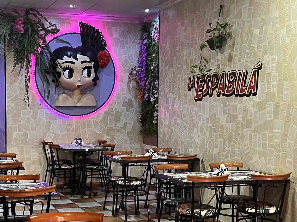 Mural de la mascota flamenca con aro de neón rosa y rótulo de La Espabilá sobre pared de papel de periódico